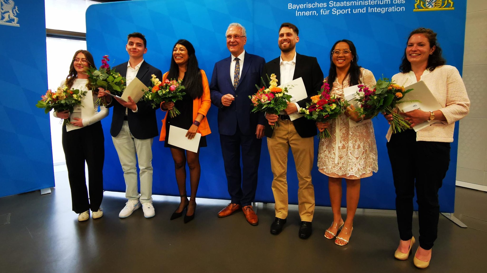 Frauen und Männer mit Blumensträußen und Einbürgerungsurkunden